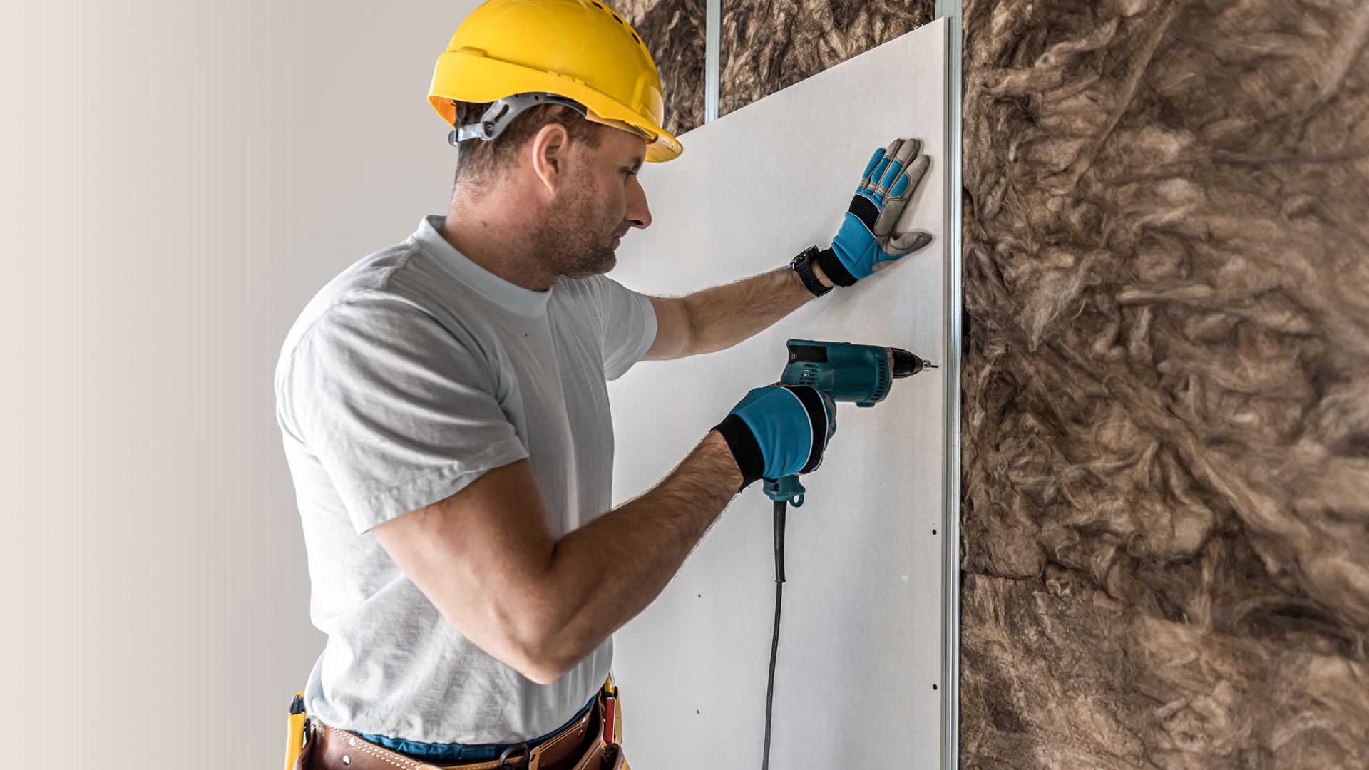 A man is using a drill to install insulation on a wall.