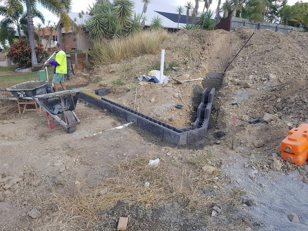 A Man is Standing Next to a Wheelbarrow in a Dirt Field — Lynams Landscapes Pty Ltd in Jensen, QLD