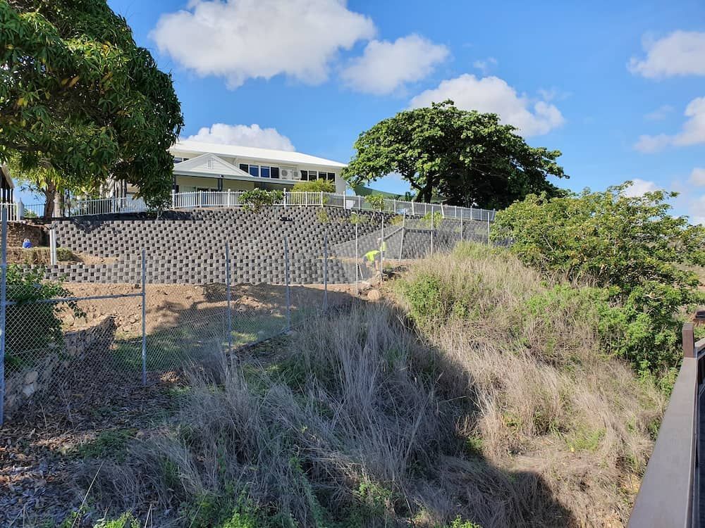 A House is Sitting on Top of a Hill Behind a Chain Link Fence — Lynams Landscapes Pty Ltd in Cosgrove, QLD