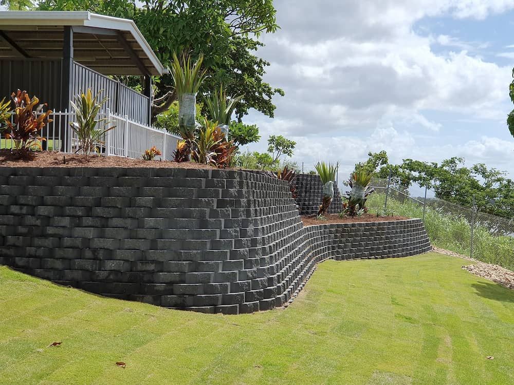 A Large Brick Wall Surrounds a House on a Hillside — Lynams Landscapes Pty Ltd in Cosgrove, QLD