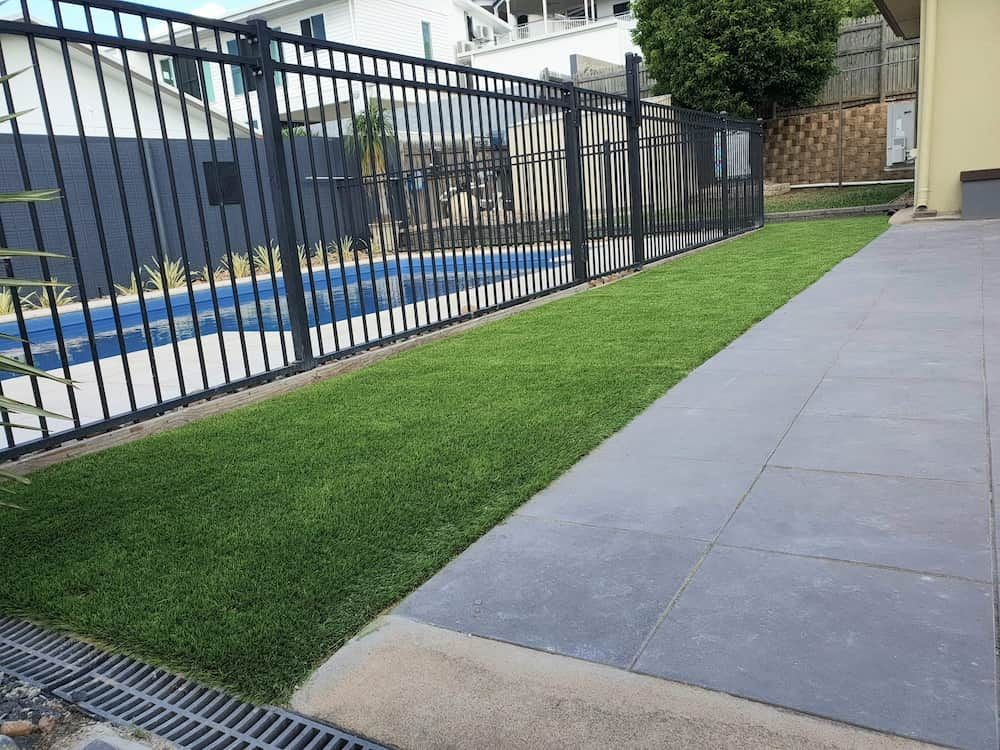 A fEnce Surrounds a Lush Green Lawn Next to a Pool — Lynams Landscapes Pty Ltd in Douglas, QLD