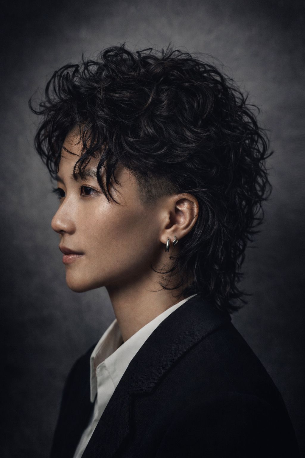 Vrouw met een grote, donkere afro, gekleed in een beige top met vetersluiting bij de halslijn, kijkt opzij.