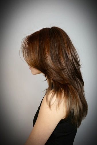 Een vrouw met lang, golvend bruin haar, gekleed in een witte crop top en jeans, poseert voor een roze muur.