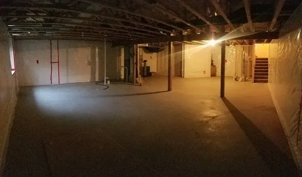 Empty unfinished basement with concrete floor, wooden beams, and support posts.
