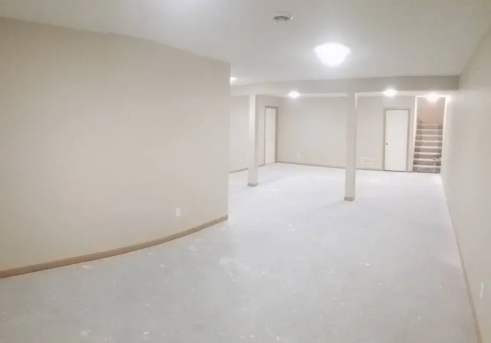 Empty, unfinished basement with neutral walls, support columns, and bare concrete floor.