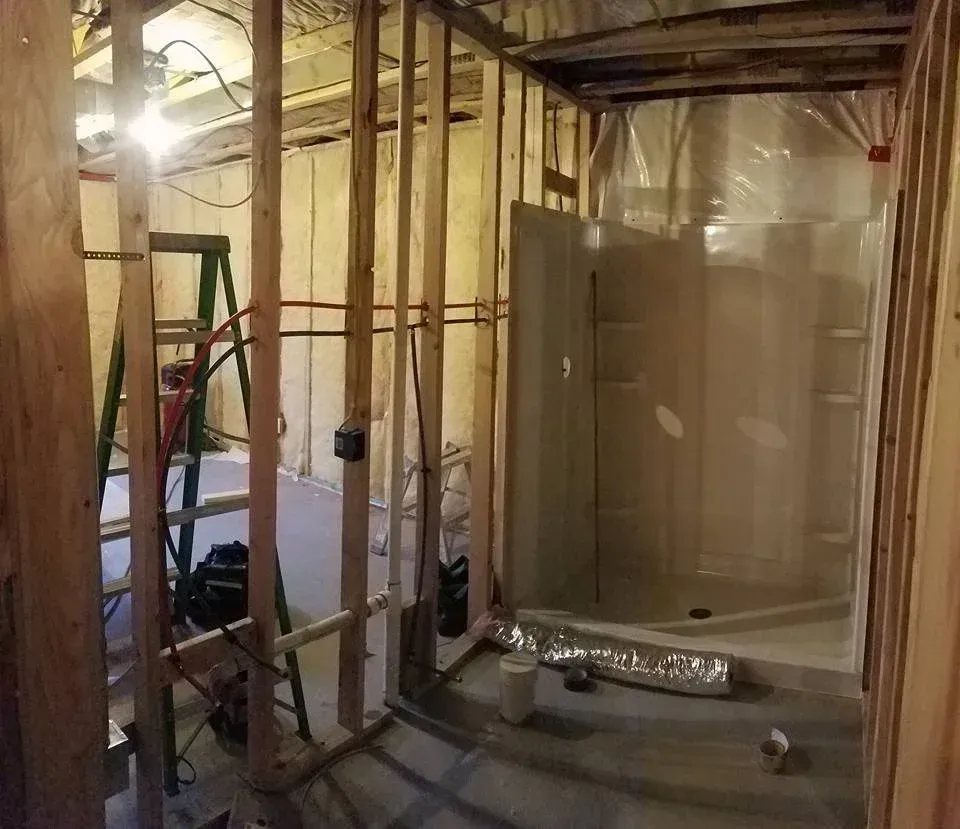 Bathroom under construction with wooden studs, shower stall, and ladder.