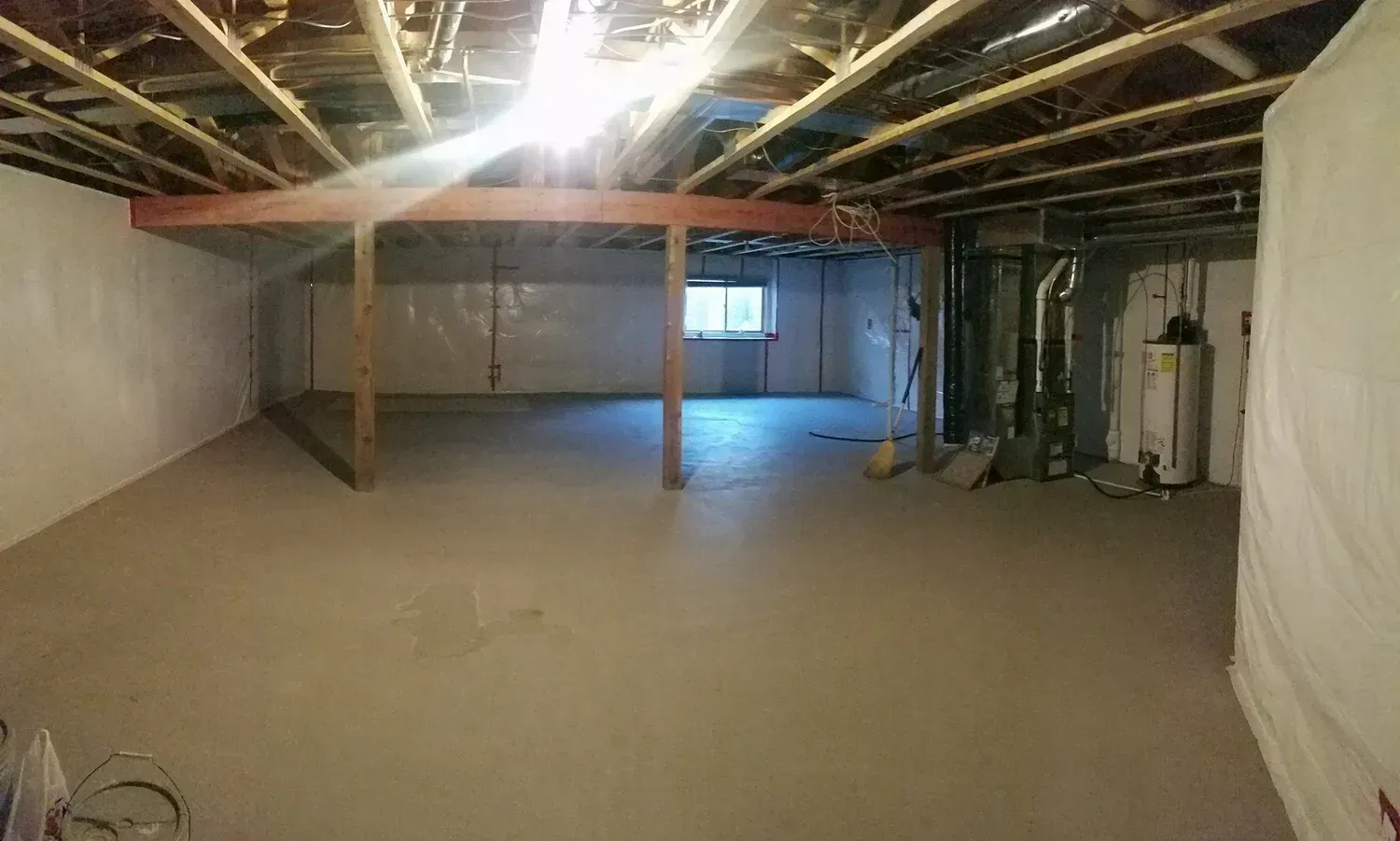 Empty unfinished basement with concrete floor, support beams, and utilities visible.