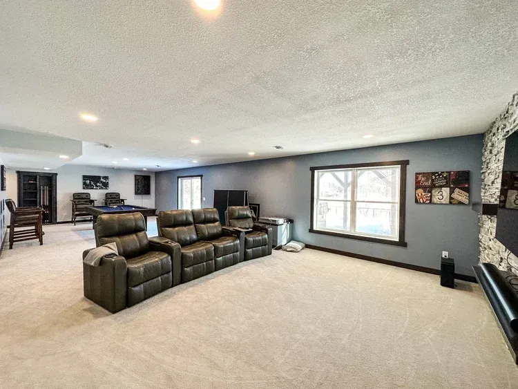 A finished basement with a large sectional sofa, pool table, and a window. Walls are gray.