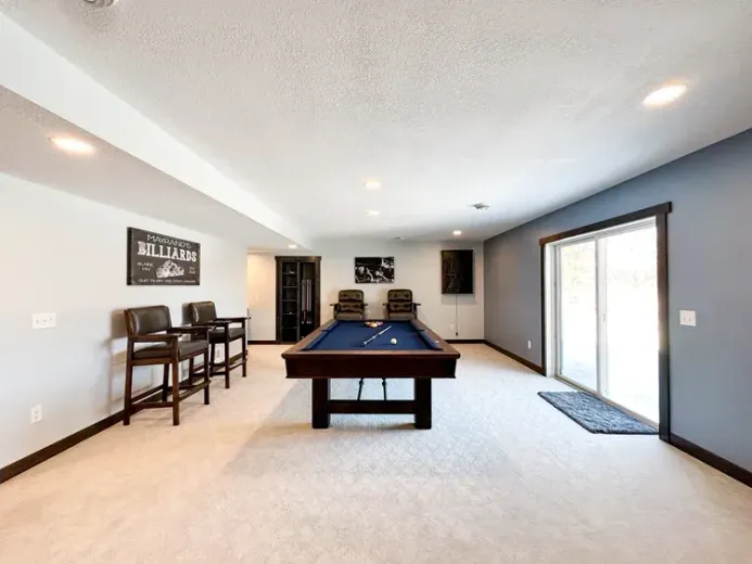 Pool table in a finished basement with a bar area, seating, and sliding glass door.