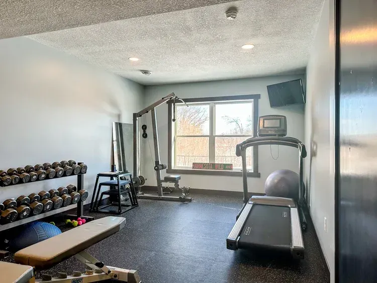Home gym with weights, treadmill, weight machine, and TV, against a light blue wall.