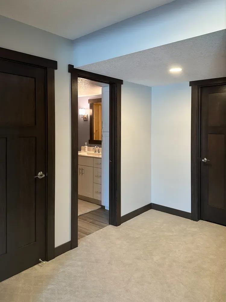 Bedroom with three dark brown doors, light blue walls, and tan carpet. One door open to a bathroom.