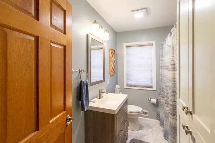 Bathroom interior with wooden door, blue walls, vanity, toilet, and shower curtain.