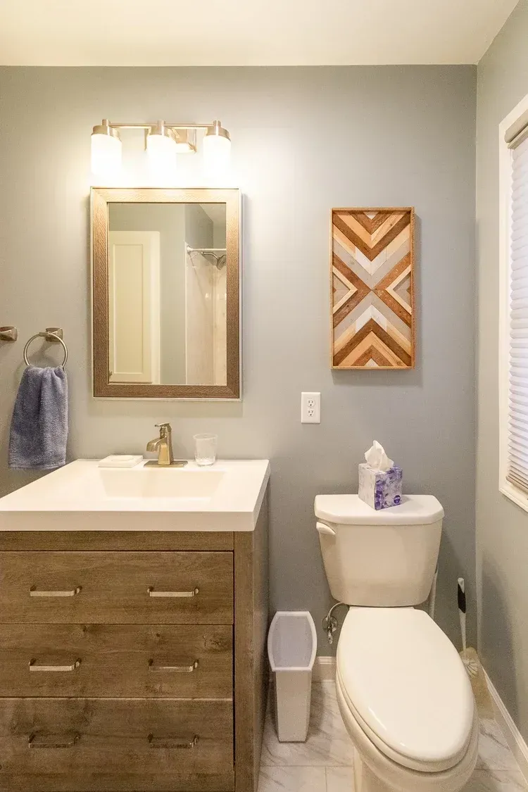 Bathroom with light blue walls, a wooden vanity, and a geometric art piece.