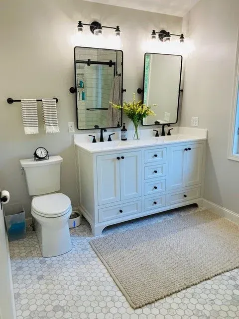 Bathroom with white vanity, black fixtures, two mirrors, and grey hexagon tile flooring.