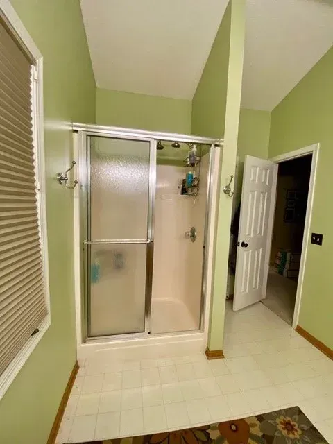 Bathroom with a shower, green walls, white tile floor, and a partially open door.