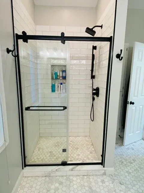 Black-framed glass shower with white subway tile walls and hex floor, a built-in shelf, and black fixtures.