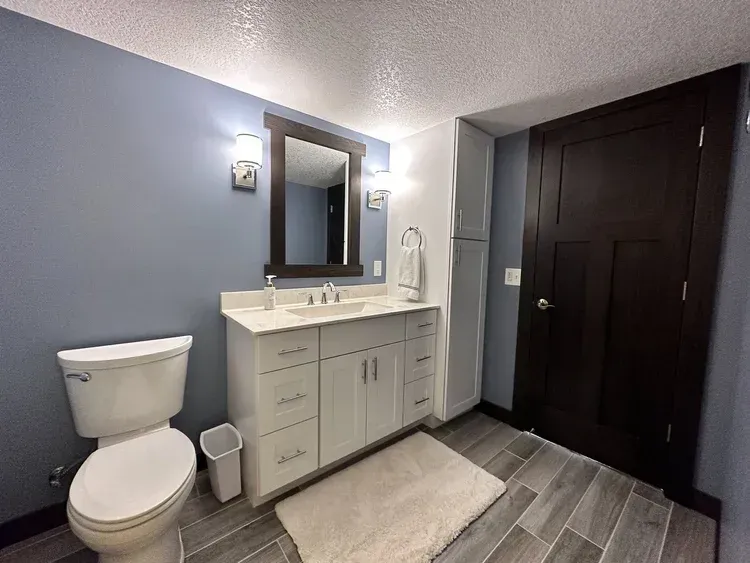 Bathroom with blue walls, white vanity, dark brown door, and gray wood-look tile floor.