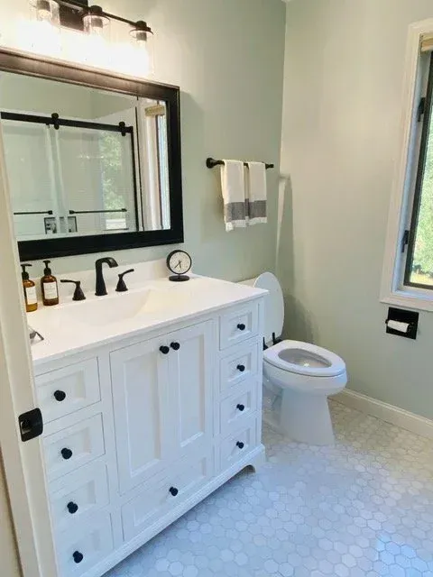 White bathroom with vanity, toilet, and hexagonal floor tiles; black accents; light green walls.