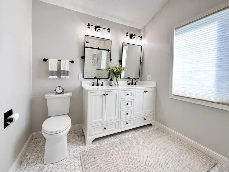 White bathroom with double vanity, mirrors, and toilet. Neutral colors.