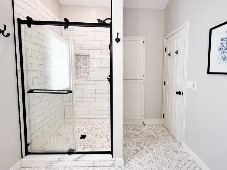 Bathroom with glass shower, white tile, white walls, and black hardware.
