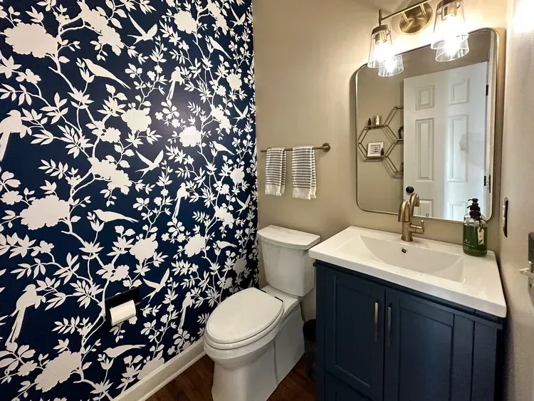 Small bathroom with blue floral wallpaper, blue vanity, and gold fixtures.