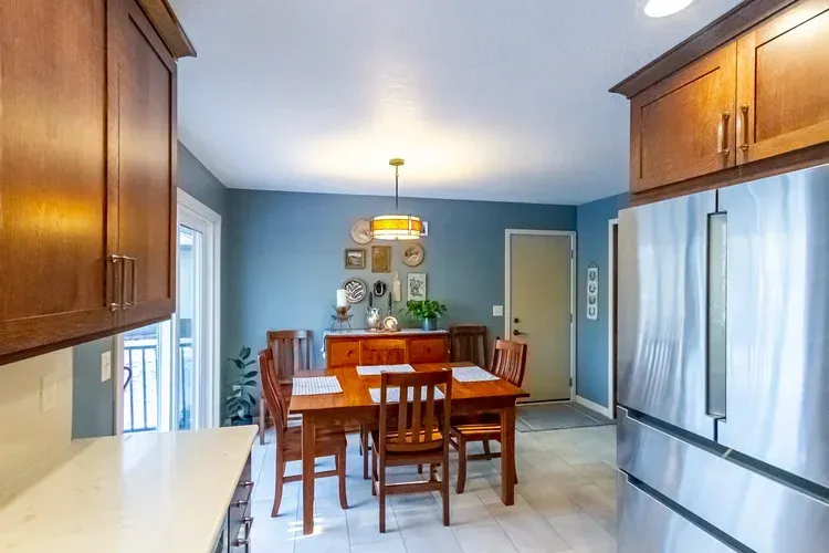 Kitchen with wooden cabinets, dining table, blue wall, and stainless steel refrigerator.