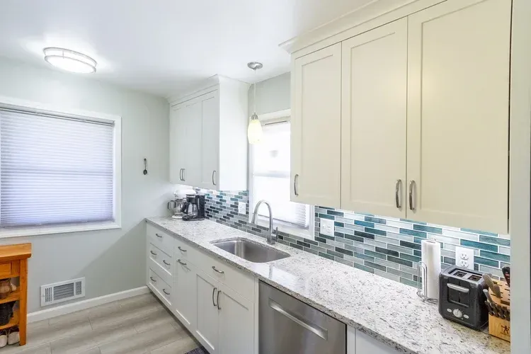 Bright kitchen with white cabinets, granite countertop, and blue-green backsplash.