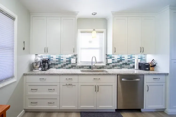 White kitchen with upper cabinets, a sink, backsplash, and a window.