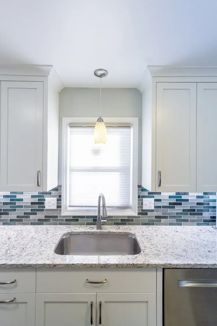 Kitchen with white cabinets, granite countertop, stainless steel sink, and blue and green mosaic backsplash.