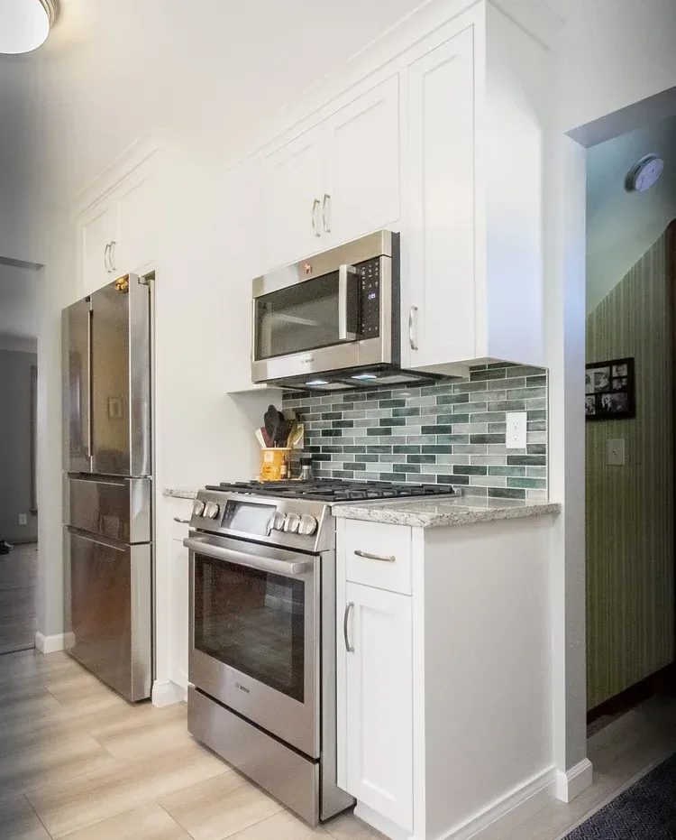 Bright, white kitchen with stainless steel appliances and a teal-tiled backsplash; the refrigerator and stove are visible.