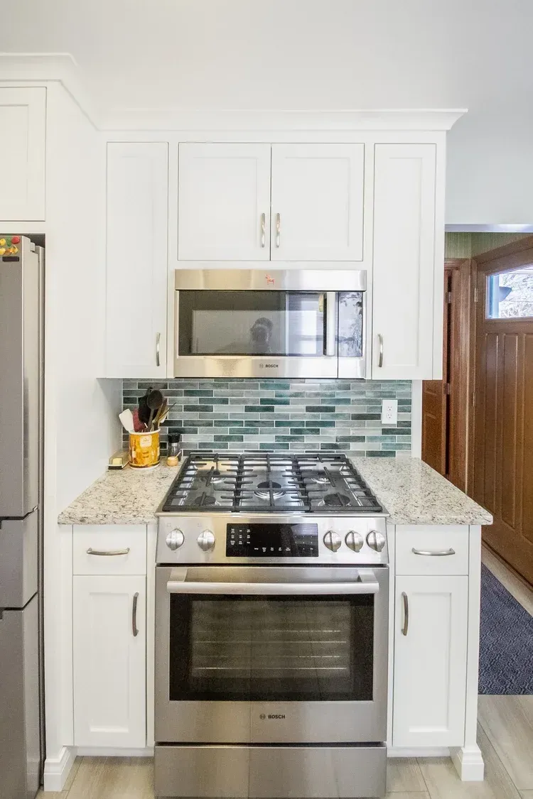 White kitchen with stainless steel stove, microwave, and cabinets. Blue-green backsplash.