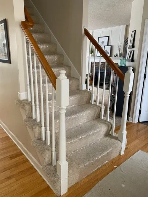 Staircase with carpeted steps, white balusters, and a wooden handrail. Sunlight streams through a nearby door.