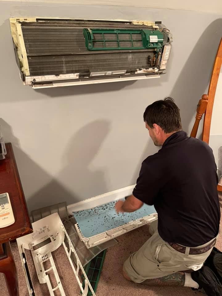 a man is kneeling down in front of a wall mounted air conditioner .