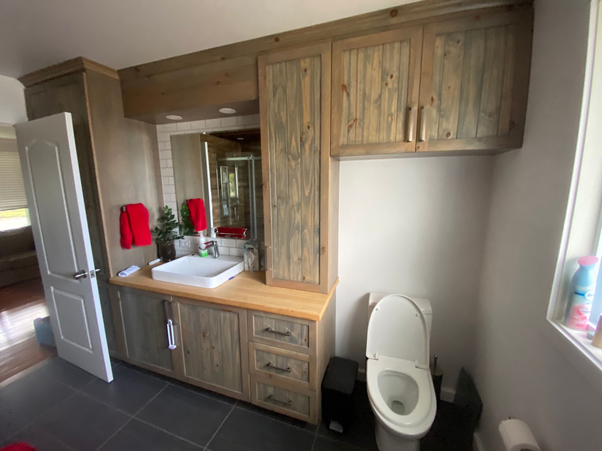 Une salle de bain avec lavabo, toilettes, miroir et armoires.