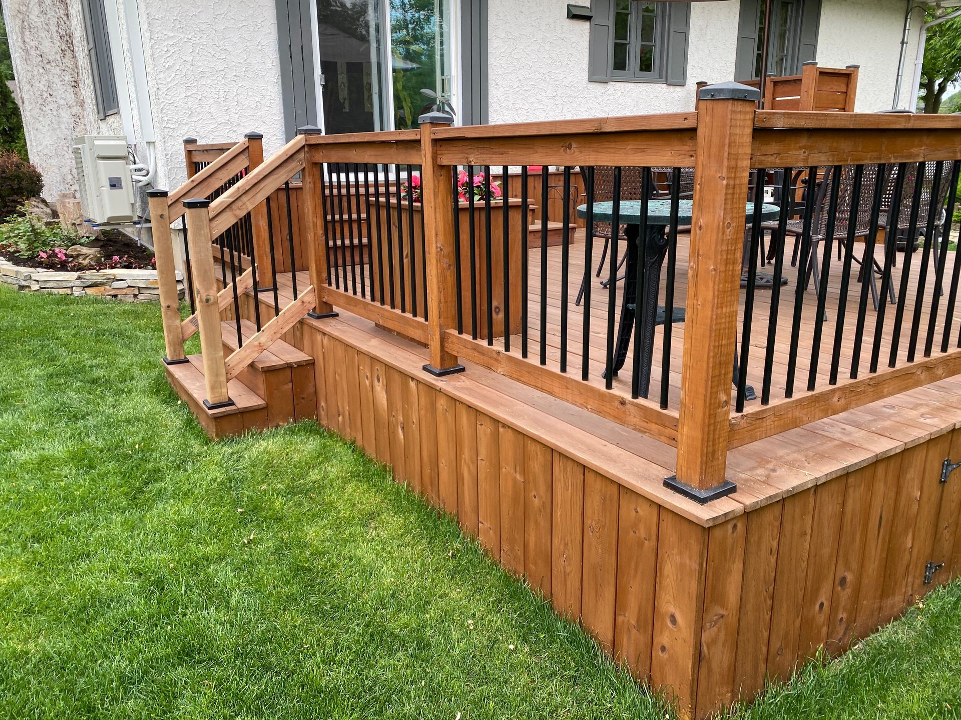 Une terrasse en bois avec une balustrade noire et des escaliers devant une maison.