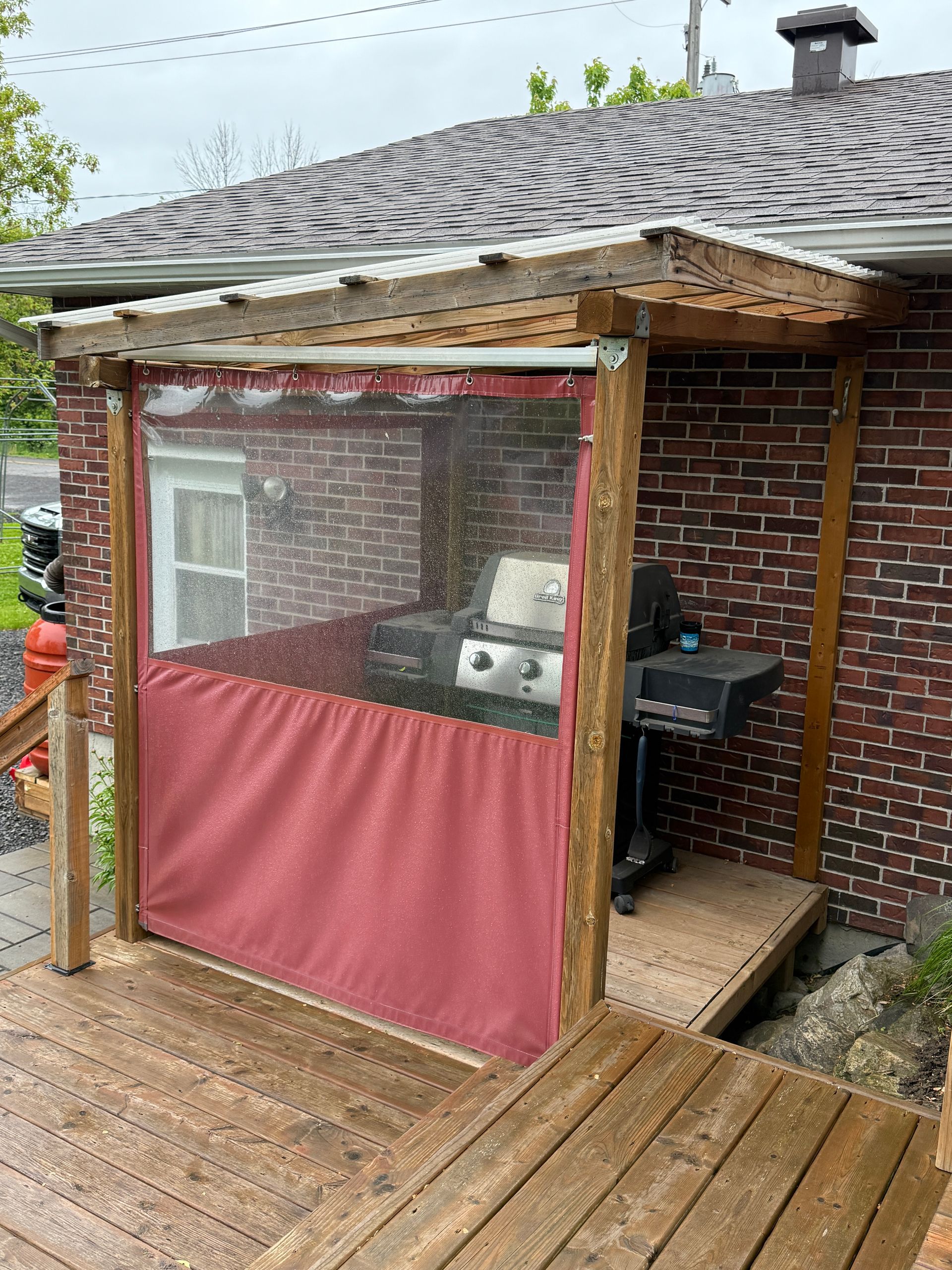Une terrasse en bois avec un gril et un rideau rouge dessus.