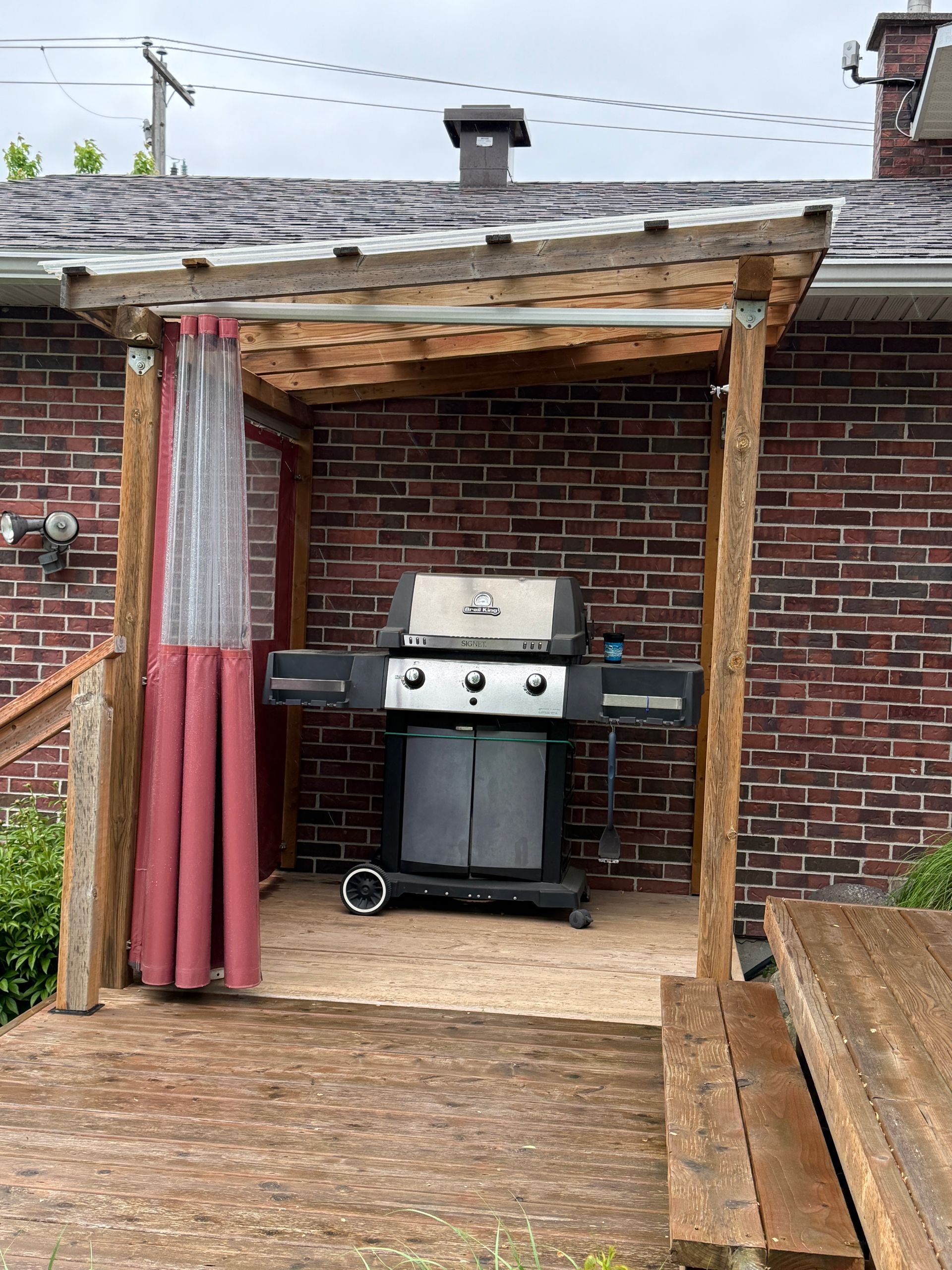 Un gril est placé sous une structure en bois devant un bâtiment en briques.