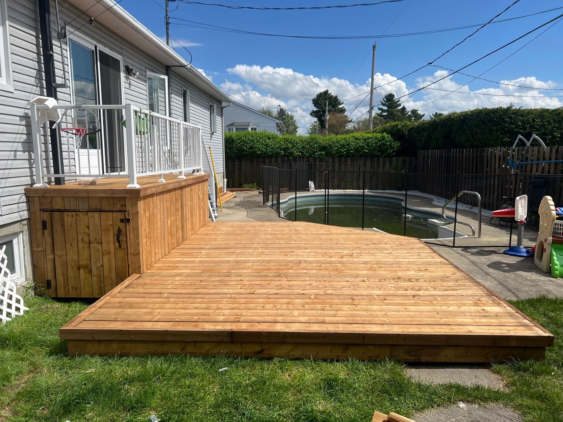 Une terrasse en bois se trouve à côté d'une piscine dans une cour arrière.