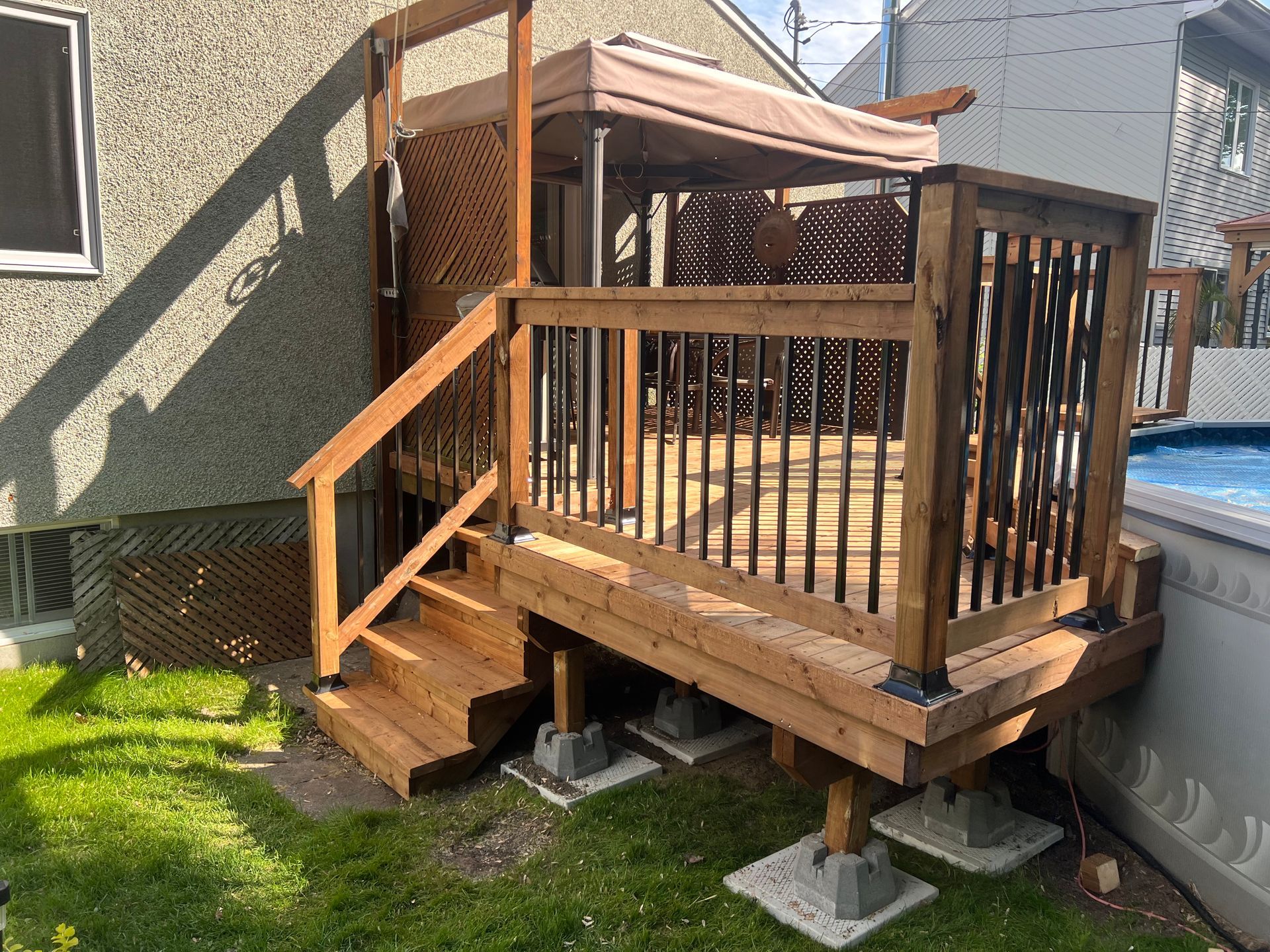 Une terrasse en bois avec des escaliers et un auvent à côté d'une piscine.