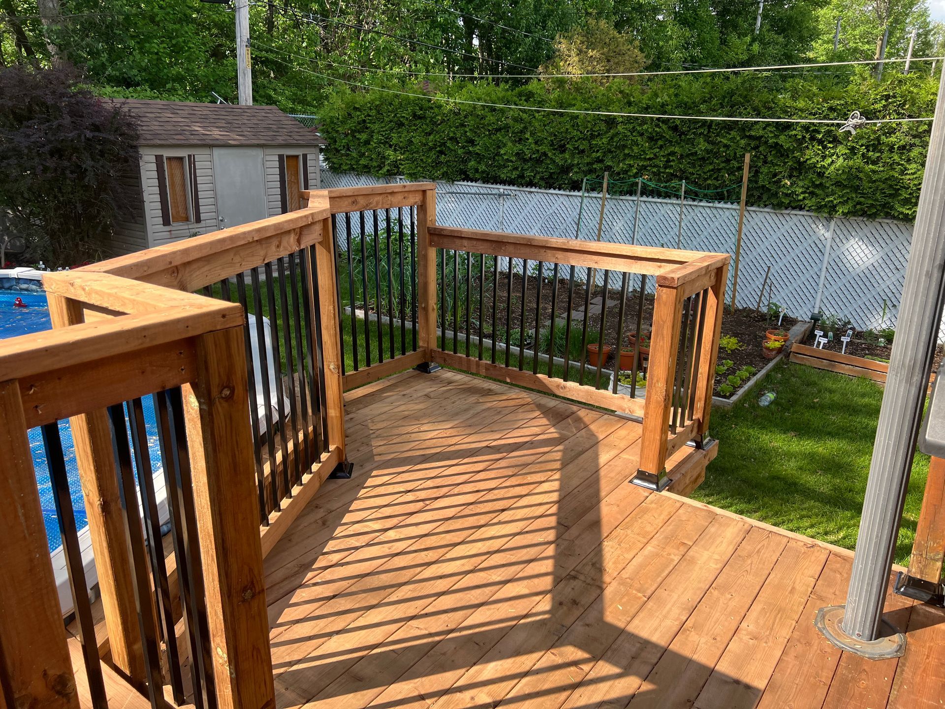Une terrasse en bois avec une balustrade en métal et des escaliers menant à une piscine.