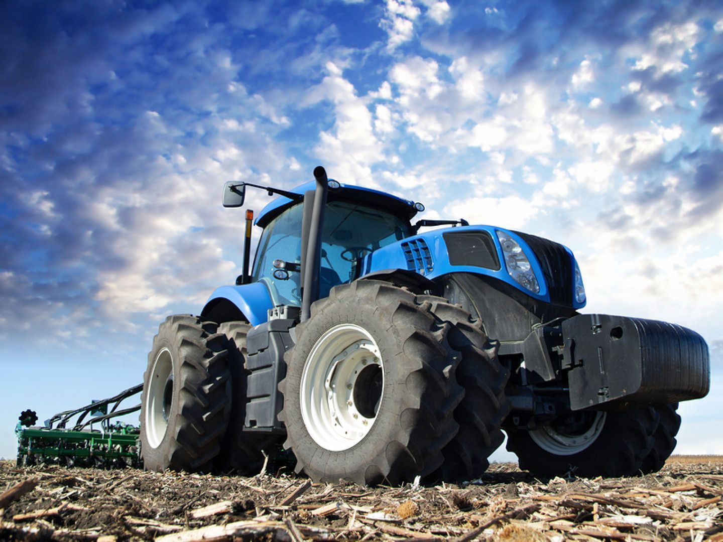 A blue tractor is plowing a field with a plow attached to it