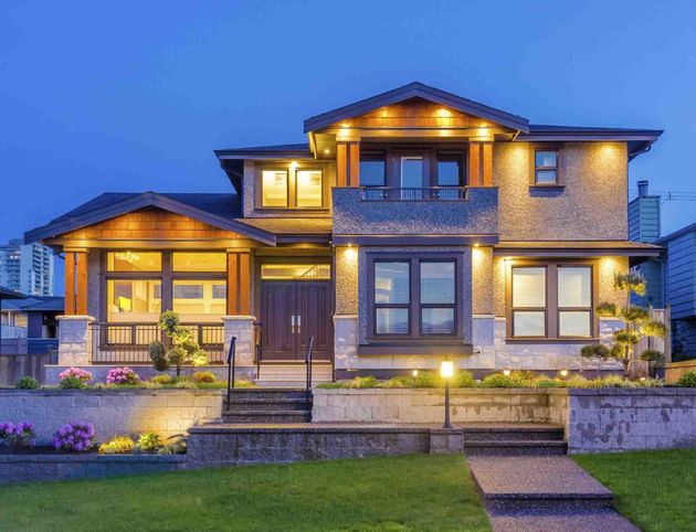 Large modern two-story house at dusk with warm lights, stone exterior, and landscaped front yard
