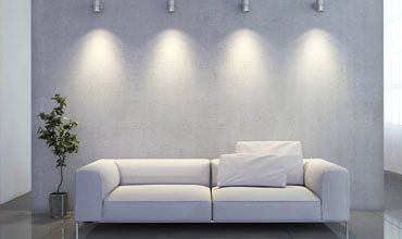 Minimalist living room with a white sofa, potted plant, and wall spotlights on a gray wall.