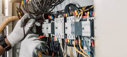 Gloved hands wiring electrical components in a control panel with tangled cables and switches