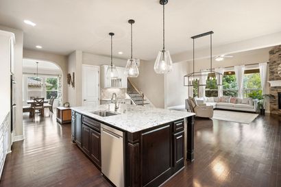 Open-concept kitchen and living room with dark wood floors, white cabinets, and pendant lights