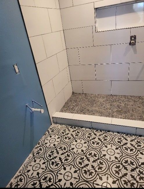 Bathroom with patterned black and white floor tiles, white tiled shower walls, and blue wall.