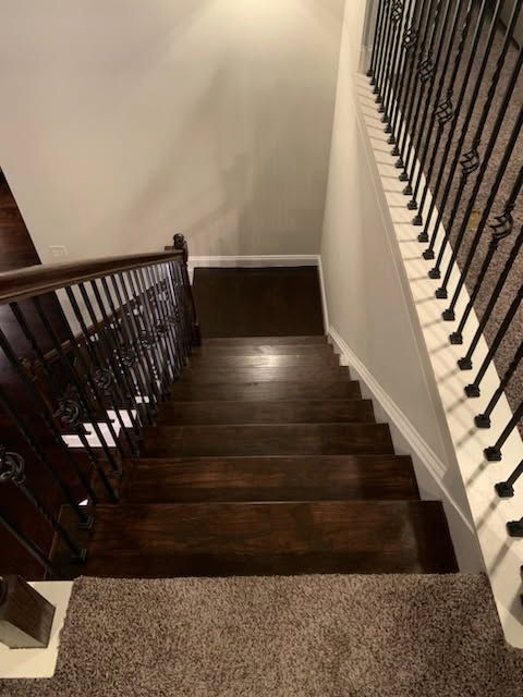 Dark wooden staircase with ornate wrought iron railing. The stairs descend to a carpeted floor.