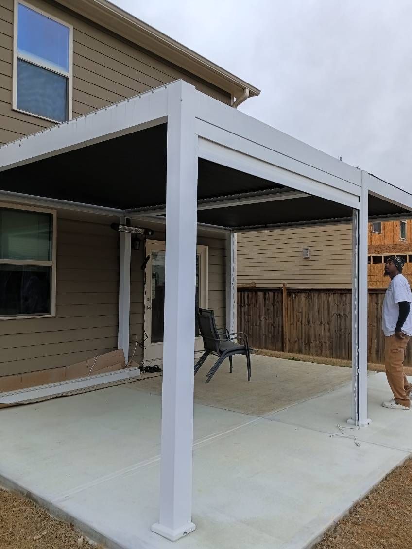 A white pergola attached to a house covers a concrete patio, a person stands near it.