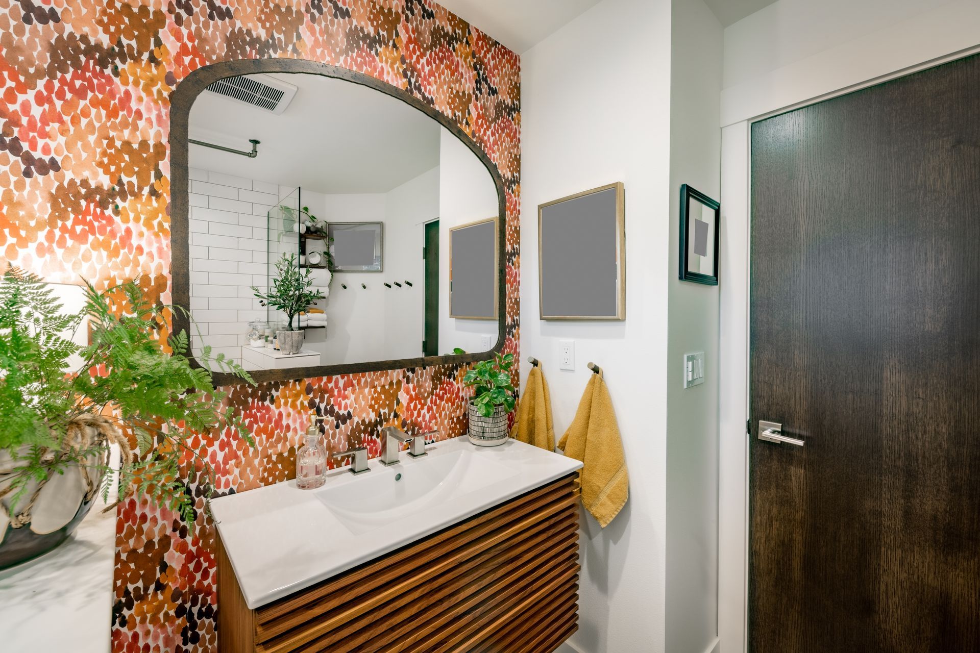Bathroom with a patterned accent wall, a wood vanity, large arched mirror, and two yellow towels hanging on the wall.