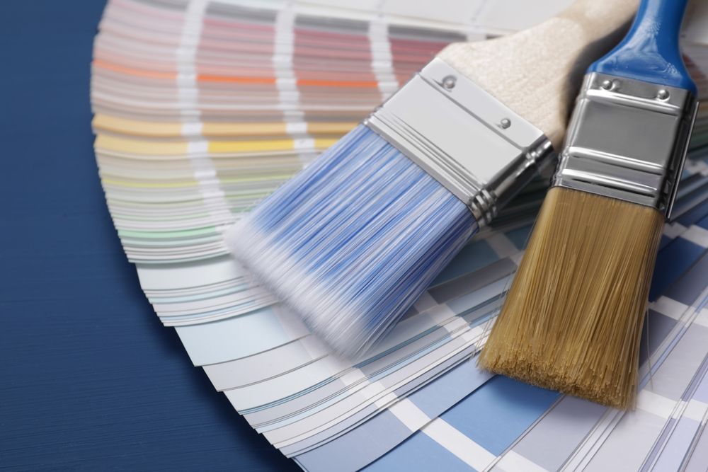 Paintbrushes resting on top of paint color swatches, showcasing various shades of blue and other colors.